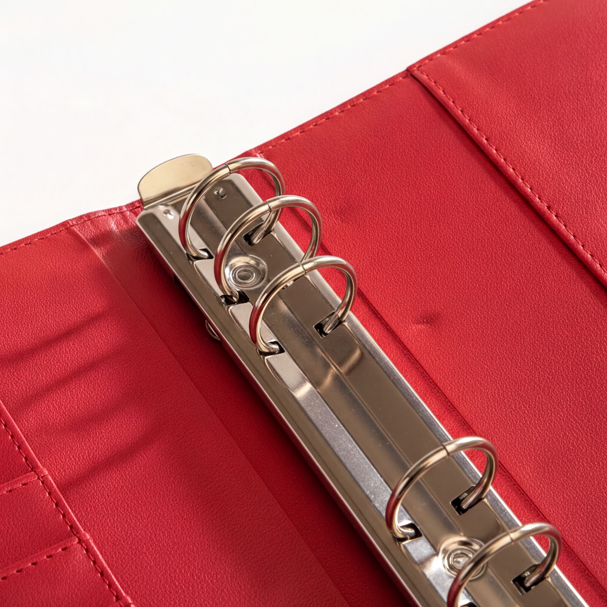A red leather-bound spiral notebook with a metal ring mechanism, open and revealing the spiral binding inside.