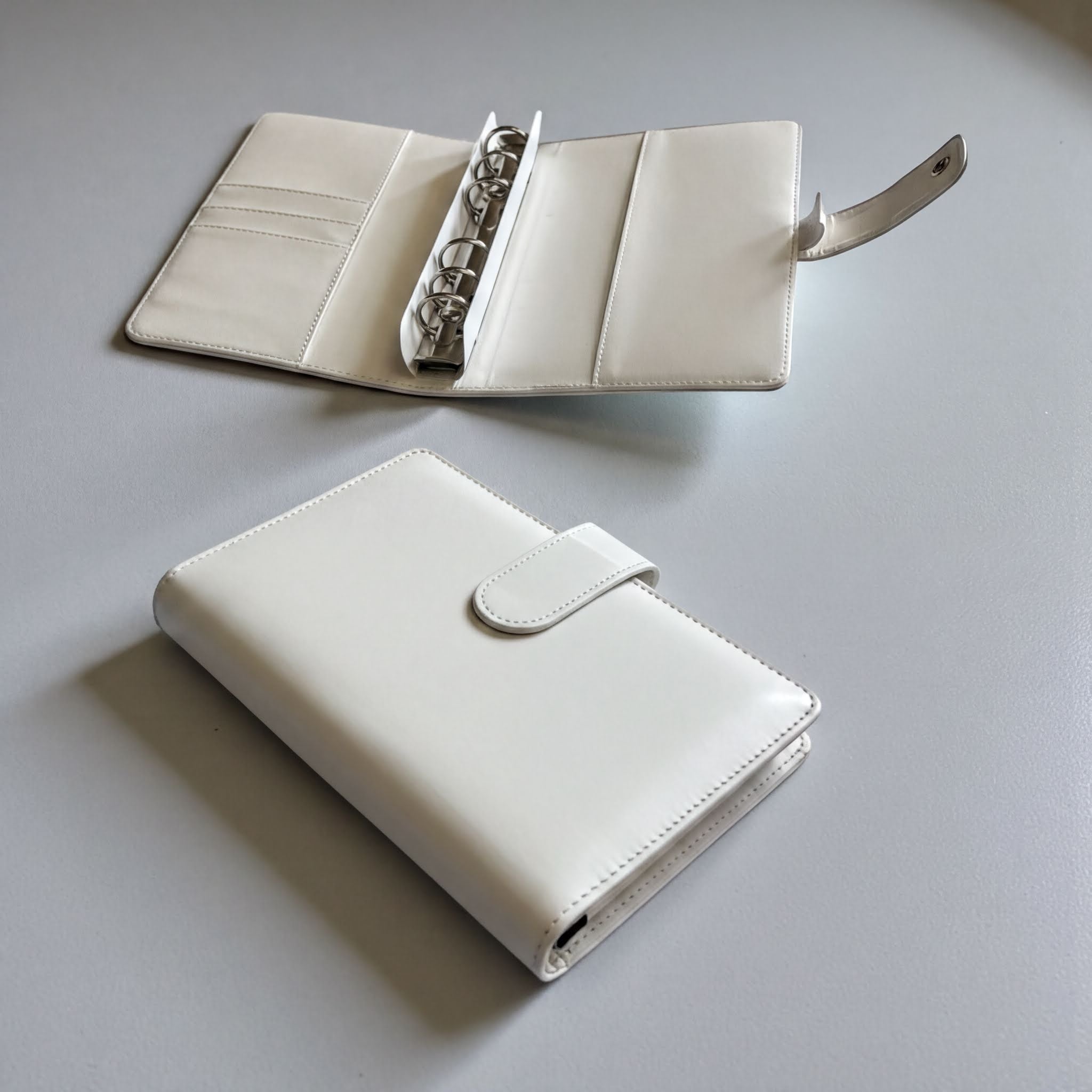 two white leather wallets or purses placed on a gray surface.