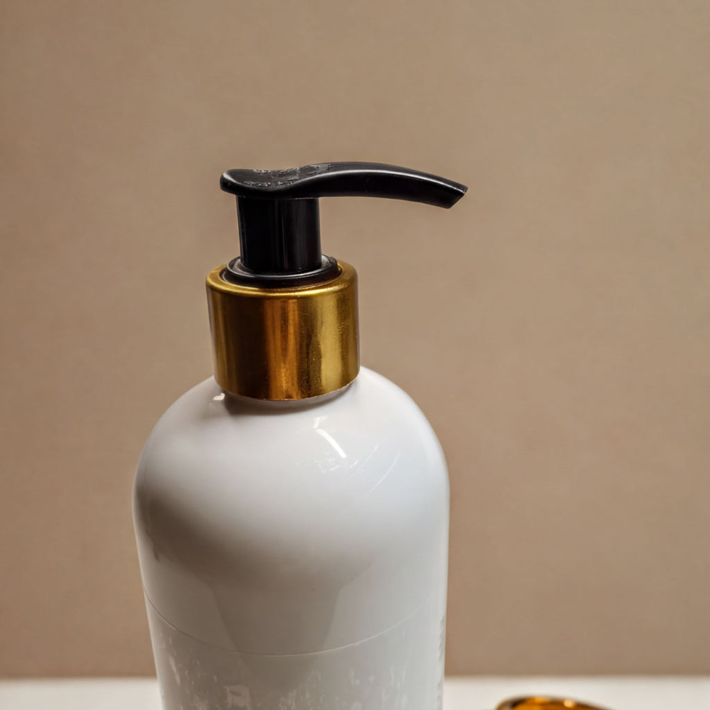 A white pump bottle with a black pump and gold-colored cap is shown against a beige background.