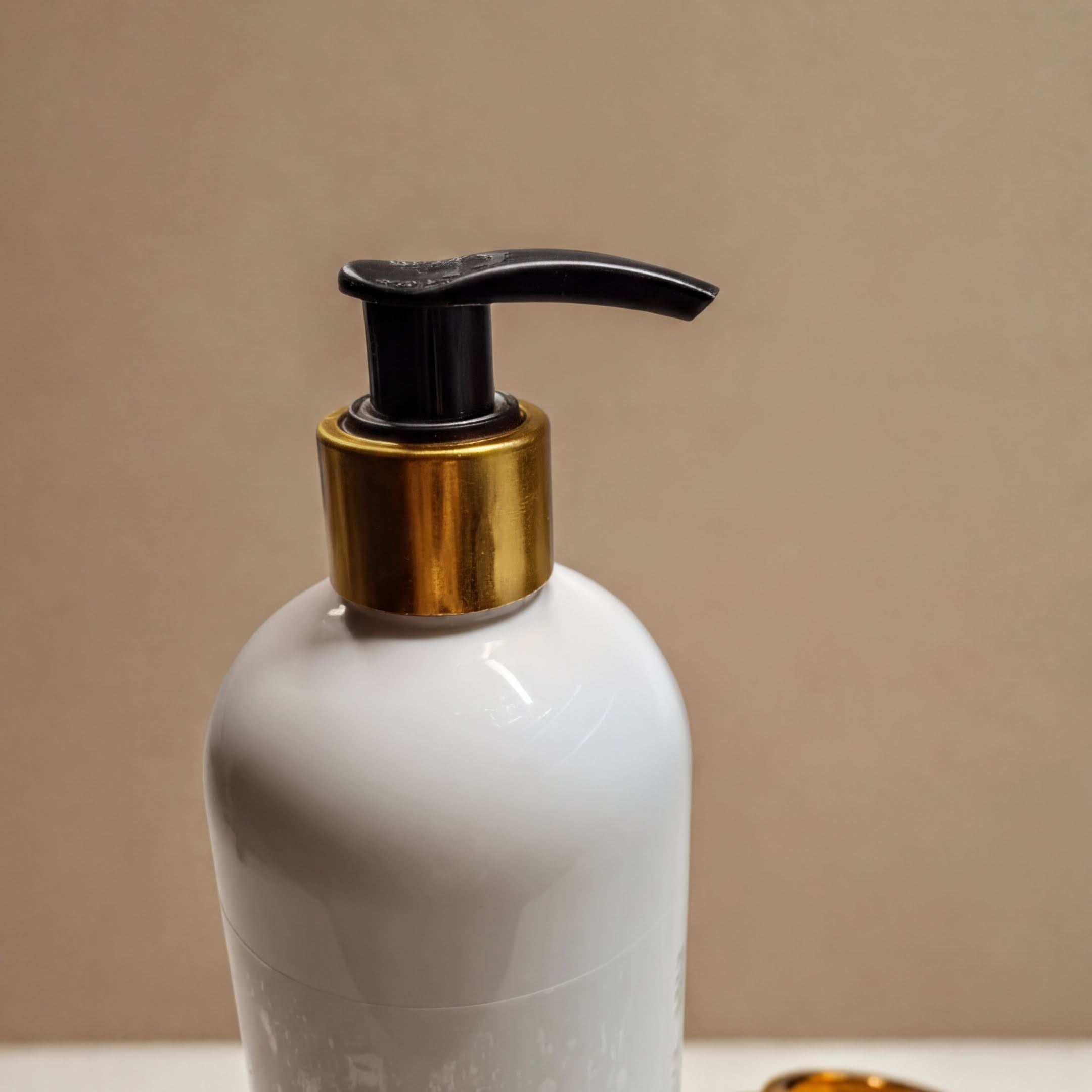 A white pump bottle with a black pump and gold-colored cap is shown against a beige background.