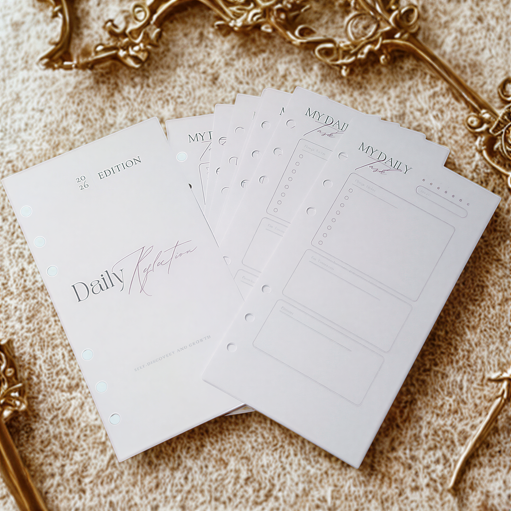 a set of planners or notebooks with a white cover and gold trim, placed on a beige surface.