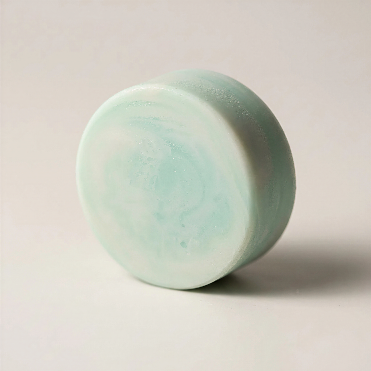A light green, round soap bar is shown against a plain white background.