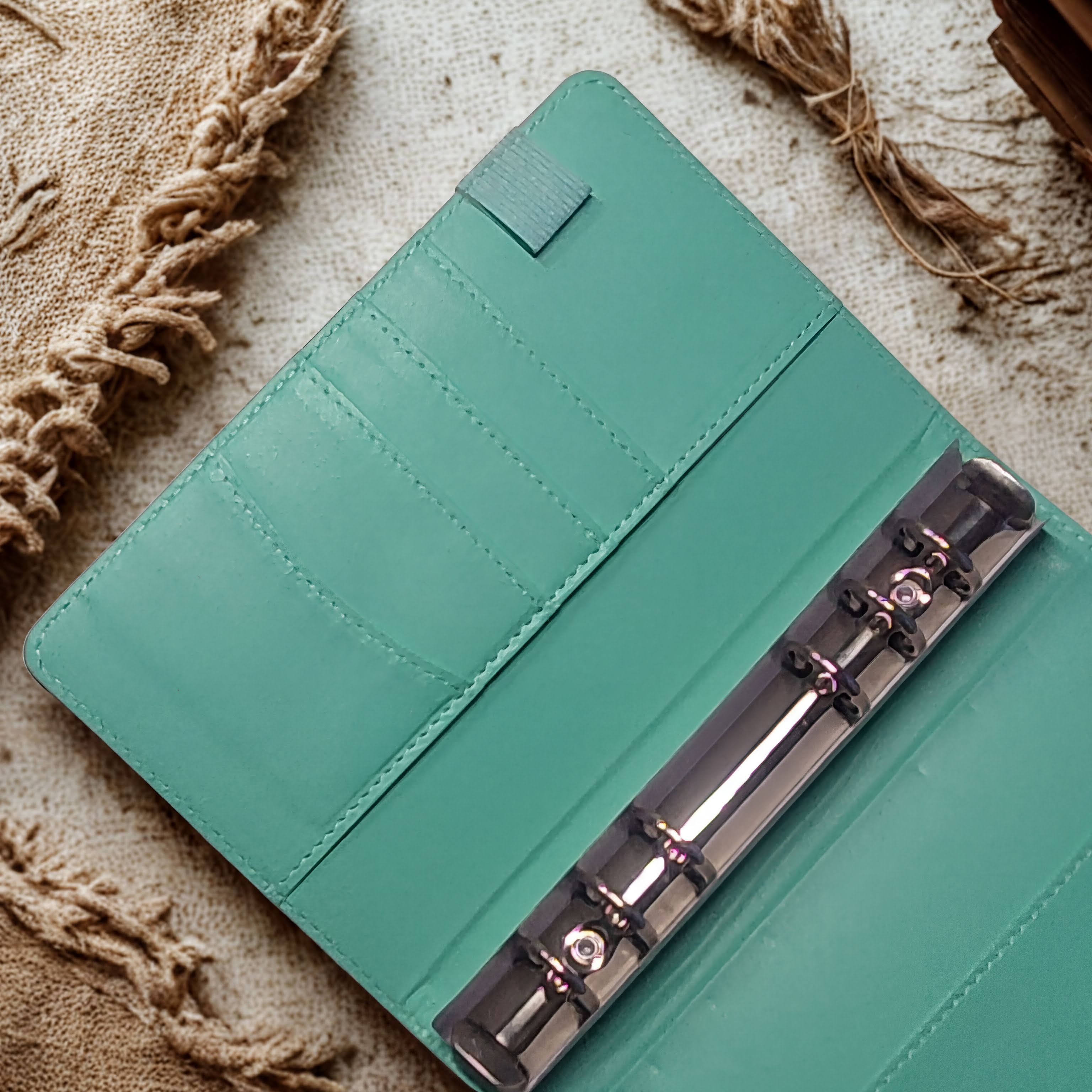 Teal leather planner with metal rings, resting on textured fabric background