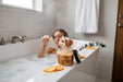 A woman is sitting in a bathtub, surrounded by orange slices and a jar of bath salt.