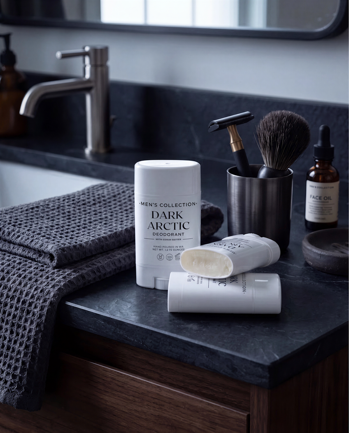 A bathroom countertop with various grooming products, including a deodorant stick, a shaving brush, and a bottle of face oil.