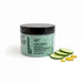 A jar of cucumber splash bath with cucumber peel and a black lid, accompanied by sliced cucumbers and a few drops of a yellow substance.