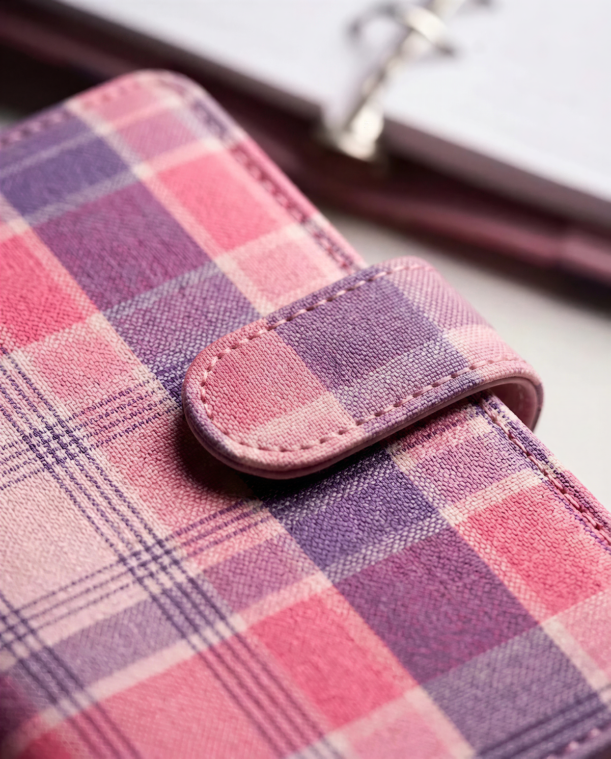 A close-up image of a pink and purple plaid wallet or purse with a clasp closure.