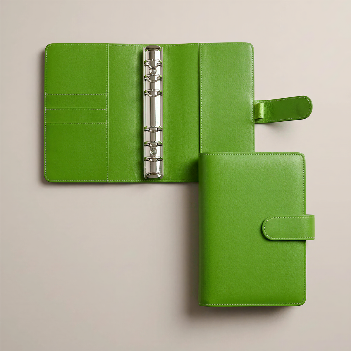 two green leather-bound notebooks or planners with metal rings, placed on a light-colored surface.