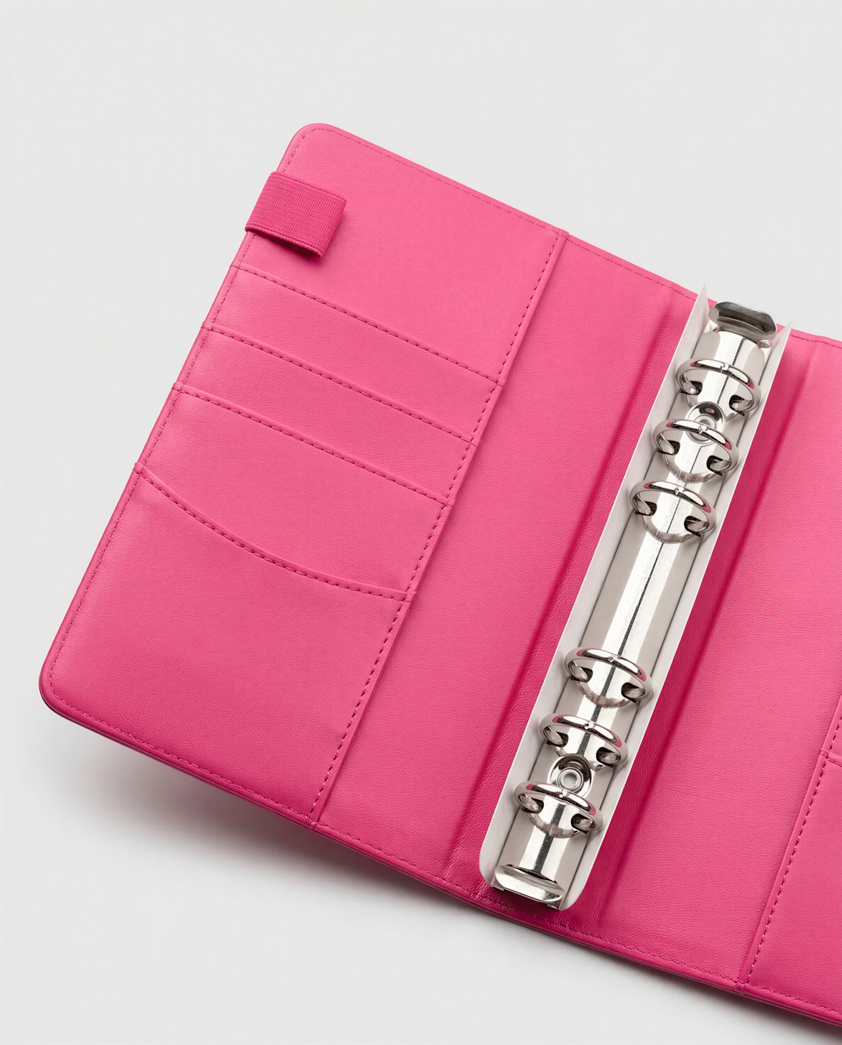 A pink leather binder with a metal ring holder inside, placed on a white surface.