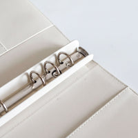A close-up view of a white leather binder with metal rings, showcasing the rings and the binder's structure.