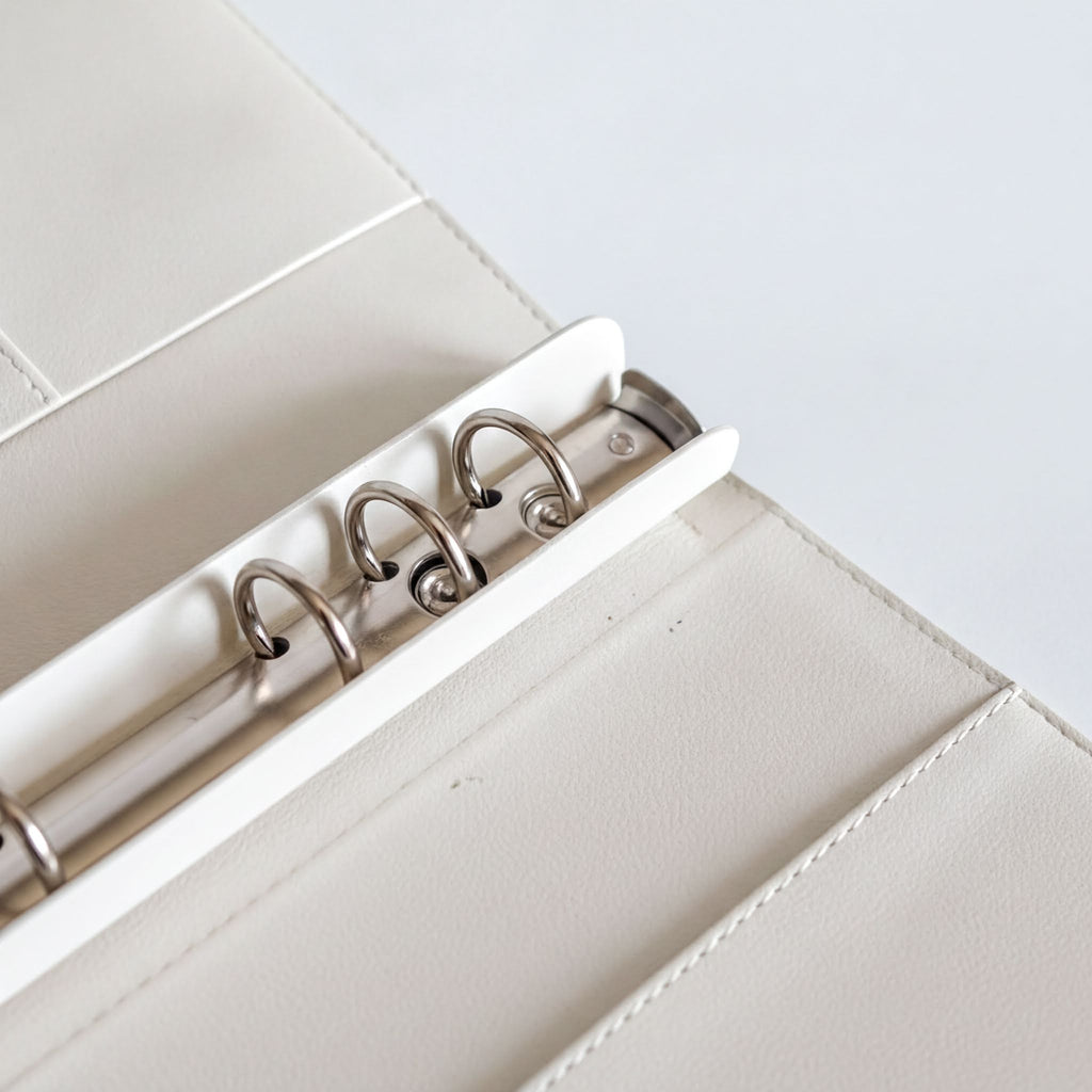 A close-up view of a white leather binder with metal rings, showcasing the rings and the binder's structure.