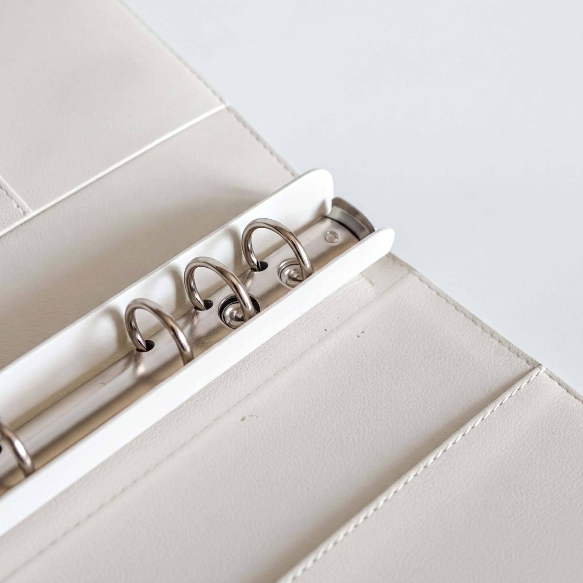 A close-up view of a white leather binder with metal rings, showcasing the rings and the binder's structure.
