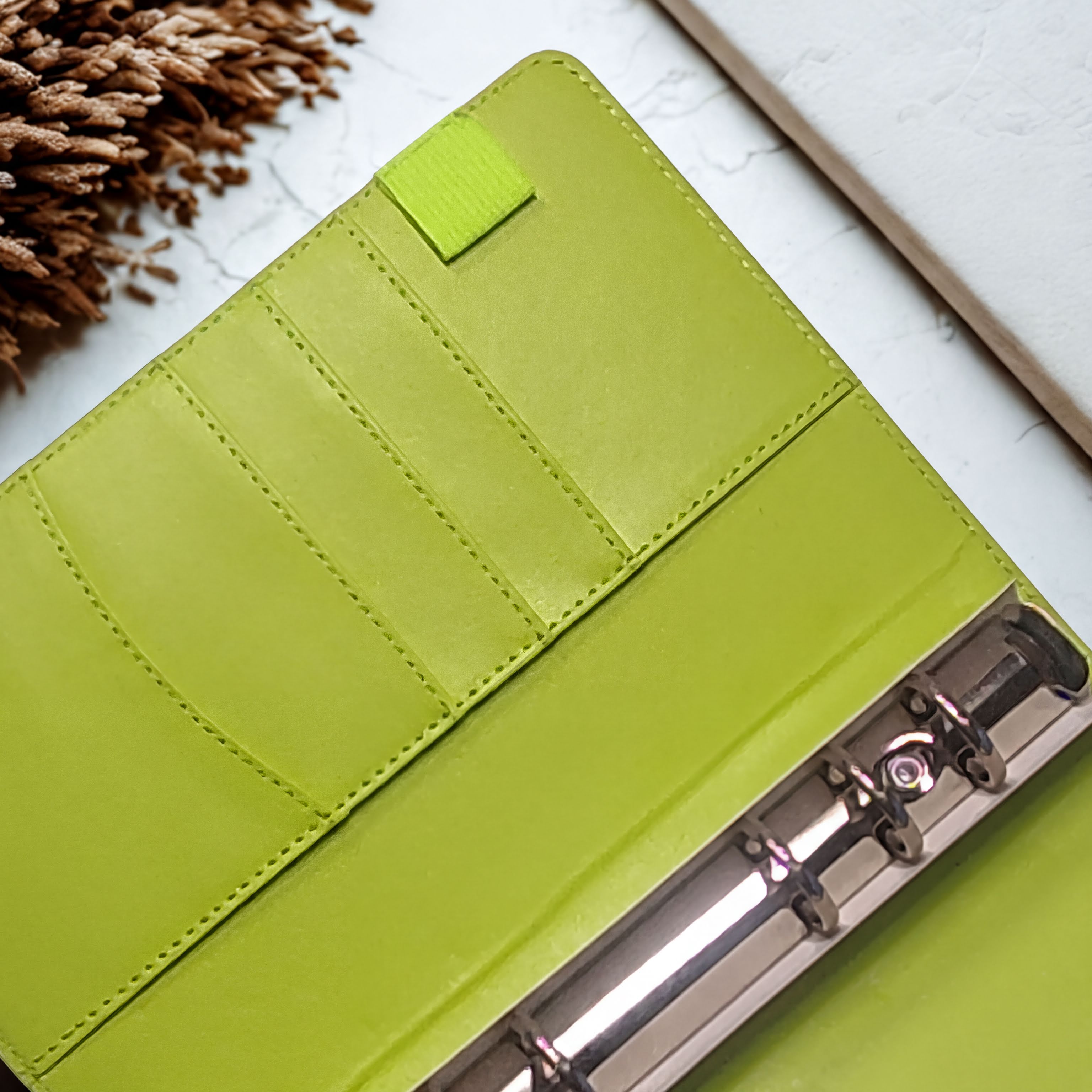 Lime green leather notebook with card slots and metal rings, styled with dried pinecone on marble