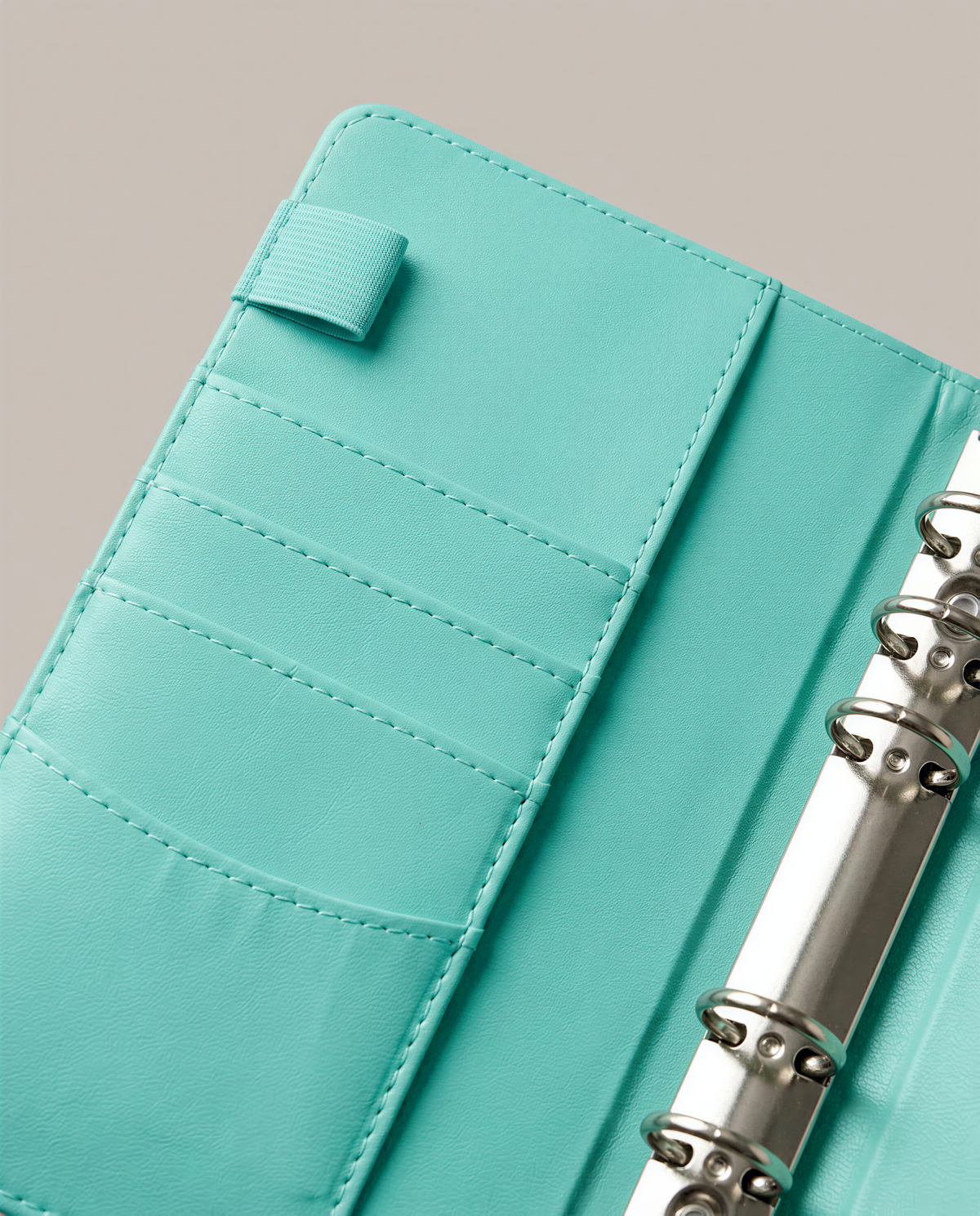 A turquoise-colored leather wallet or purse with multiple pockets and a metal ring binder attached.