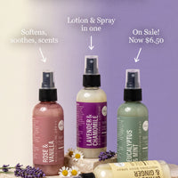 three bottles of different scented lotions and sprays, each with a different color and scent, arranged on a white surface with purple flowers.