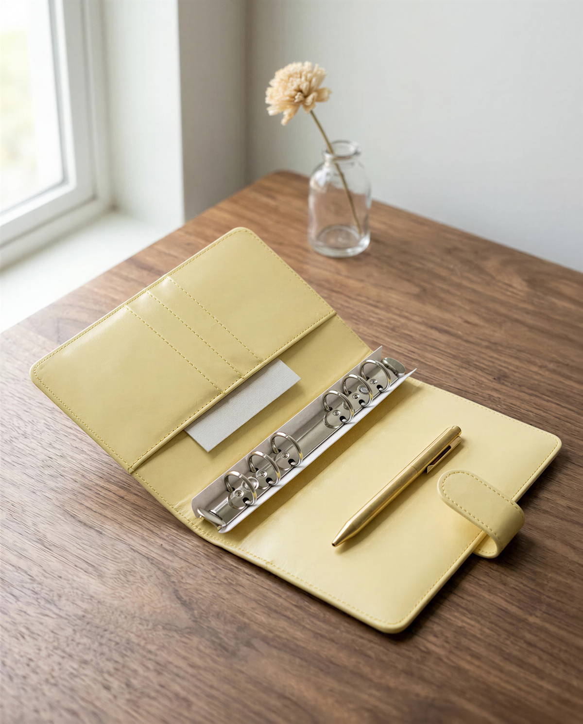 a wooden desk with a yellow leather binder, a pen, and a small vase with a single flower.