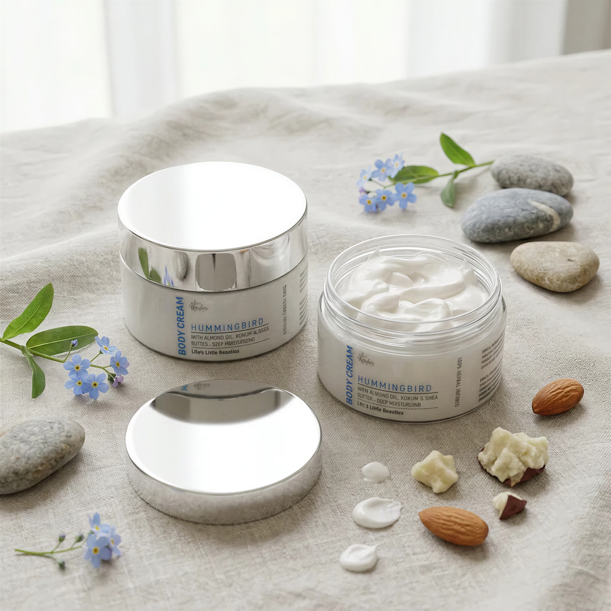 two jars of body cream, one with a lid and the other open, surrounded by various natural elements such as almonds, blue flowers, and rocks.