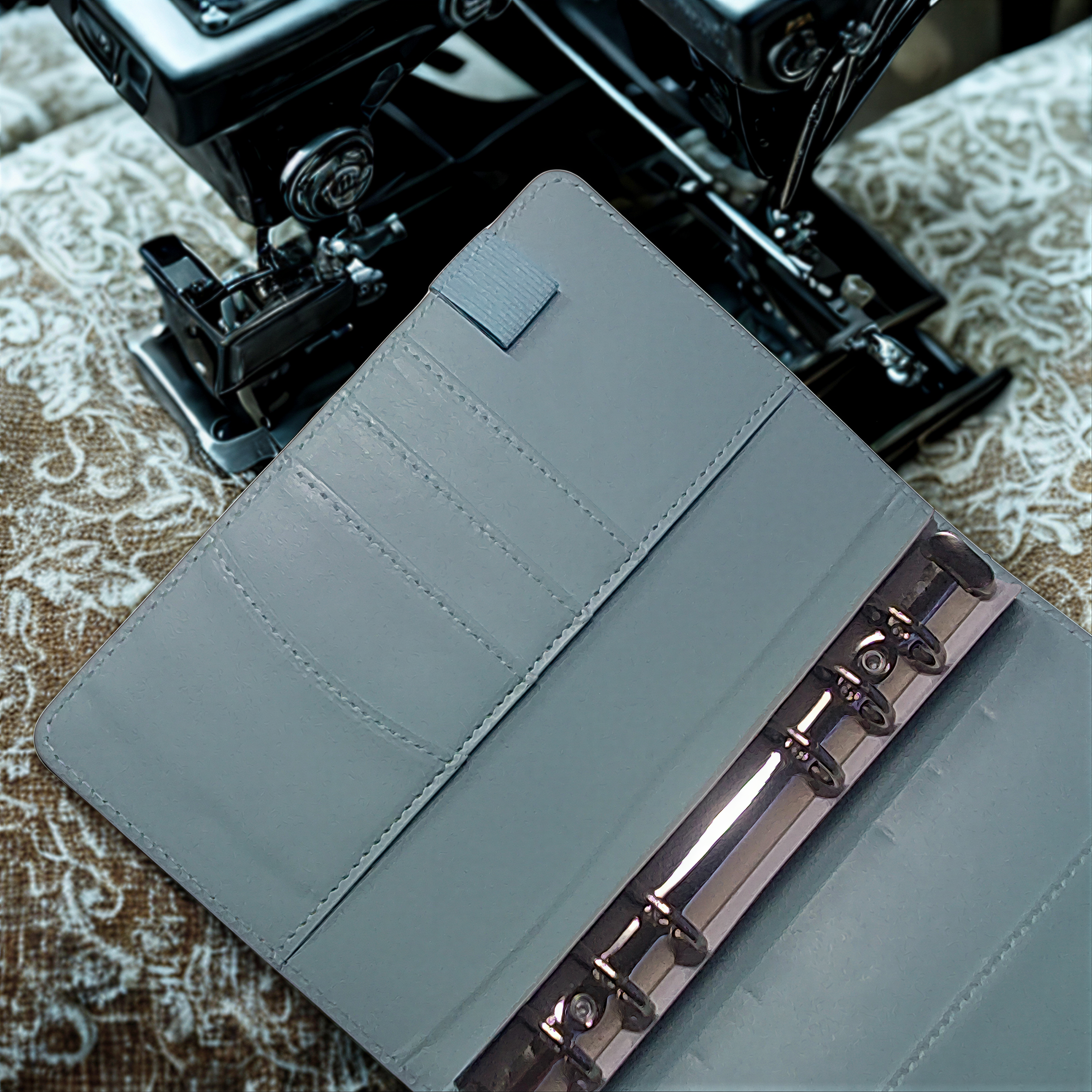 Gray leather wallet with metal clasp beside vintage sewing machine on patterned fabric