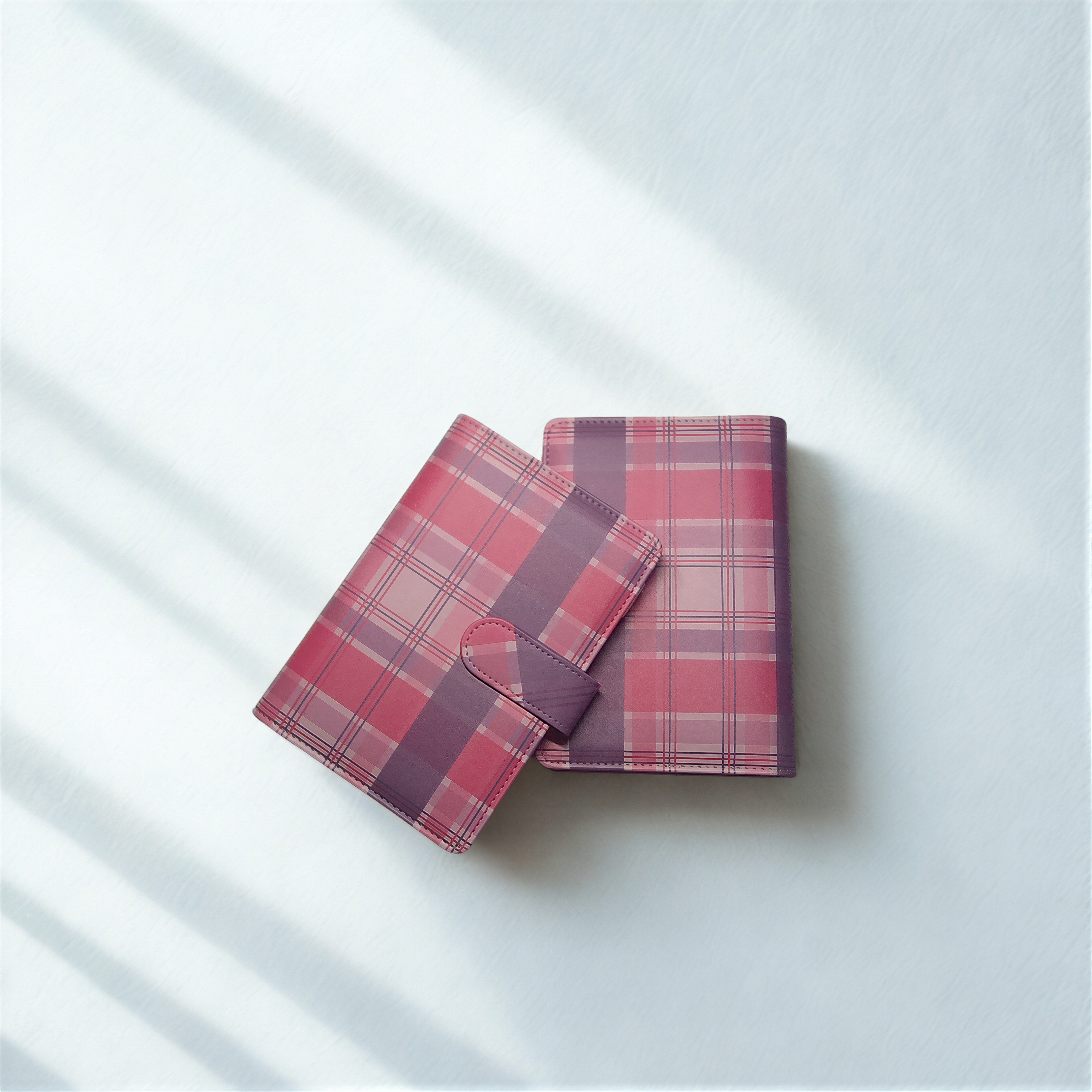 Pink and purple plaid wallets on white textured surface with soft shadows