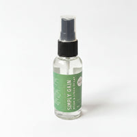 A clear glass spray bottle with a black pump, containing a clear liquid, labeled as a "Simply Gain" room spray.