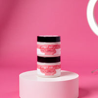 Two jars of pink hair color products are stacked on a white pedestal against a pink background.