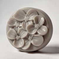 A round, gray soap dish with a floral design featuring multiple flower-shaped soap bubbles.