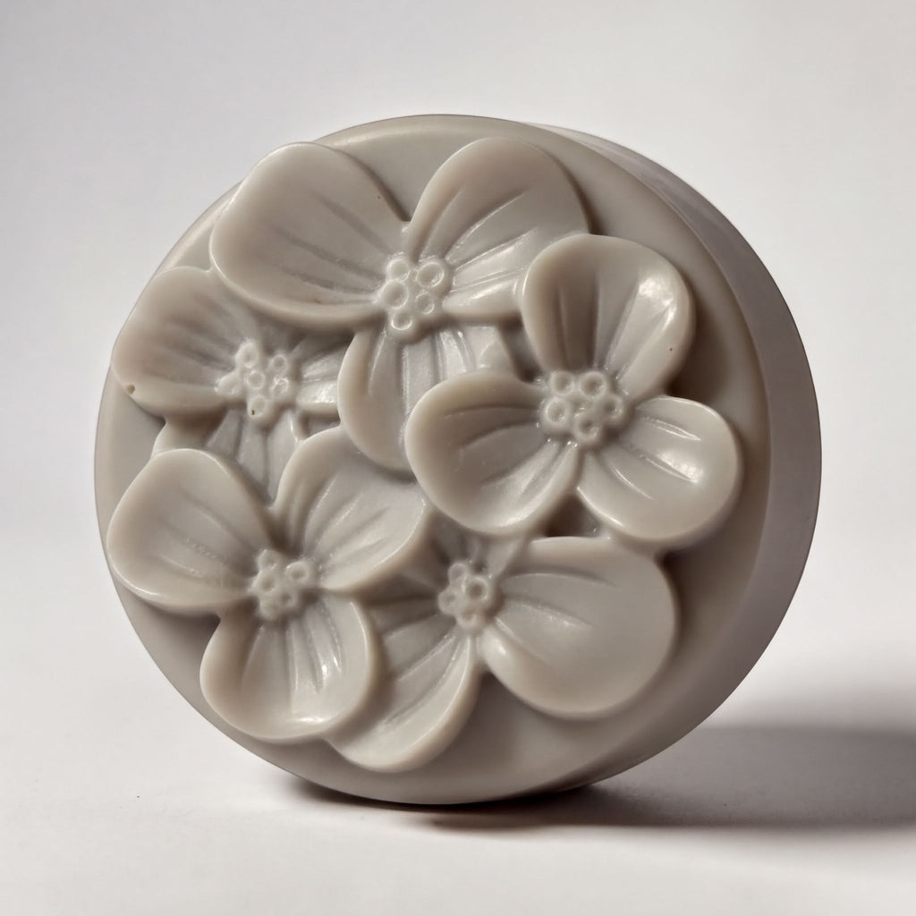 A round, gray soap dish with a floral design featuring multiple flower-shaped soap bubbles.