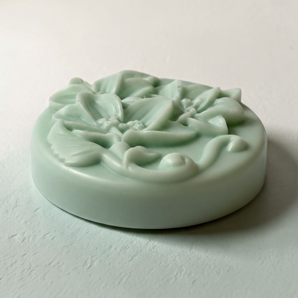 A round, light green soap bar with a floral design on it, sitting on a white surface.