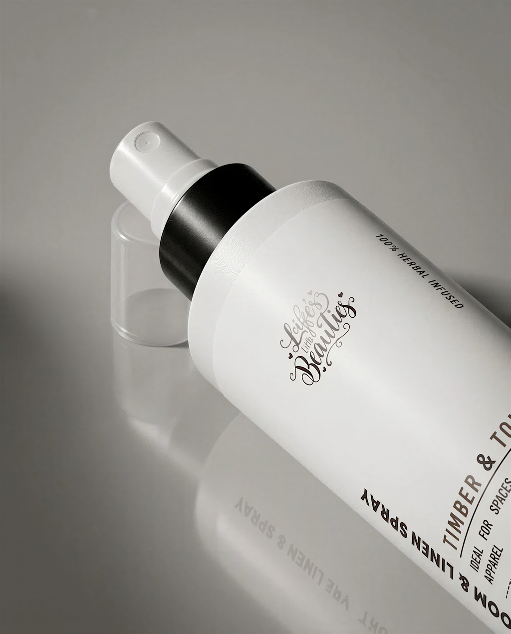 A spray bottle with a black cap and white label, resting on a reflective surface.