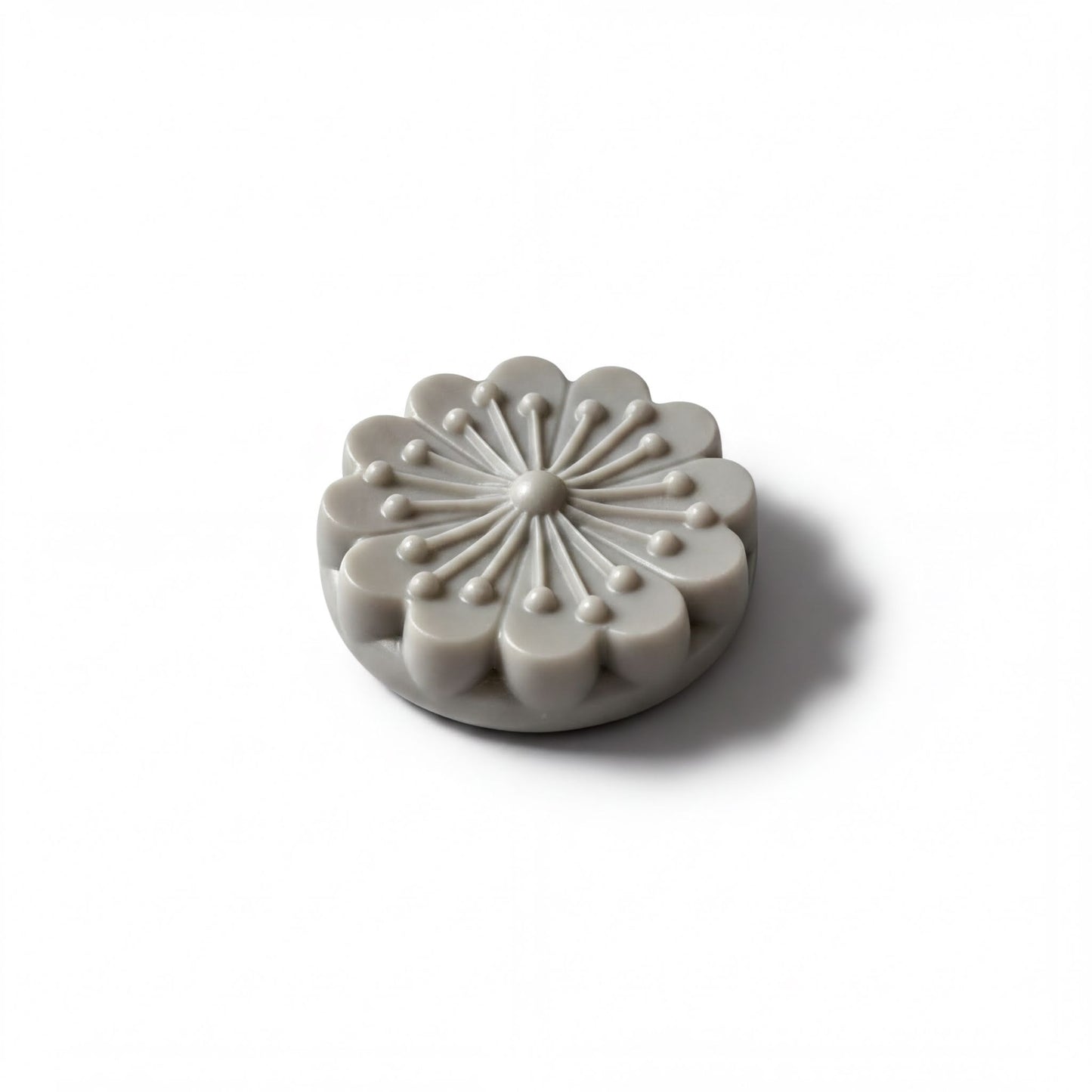 A gray, flower-shaped object with a central design and radiating petals is shown against a white background.