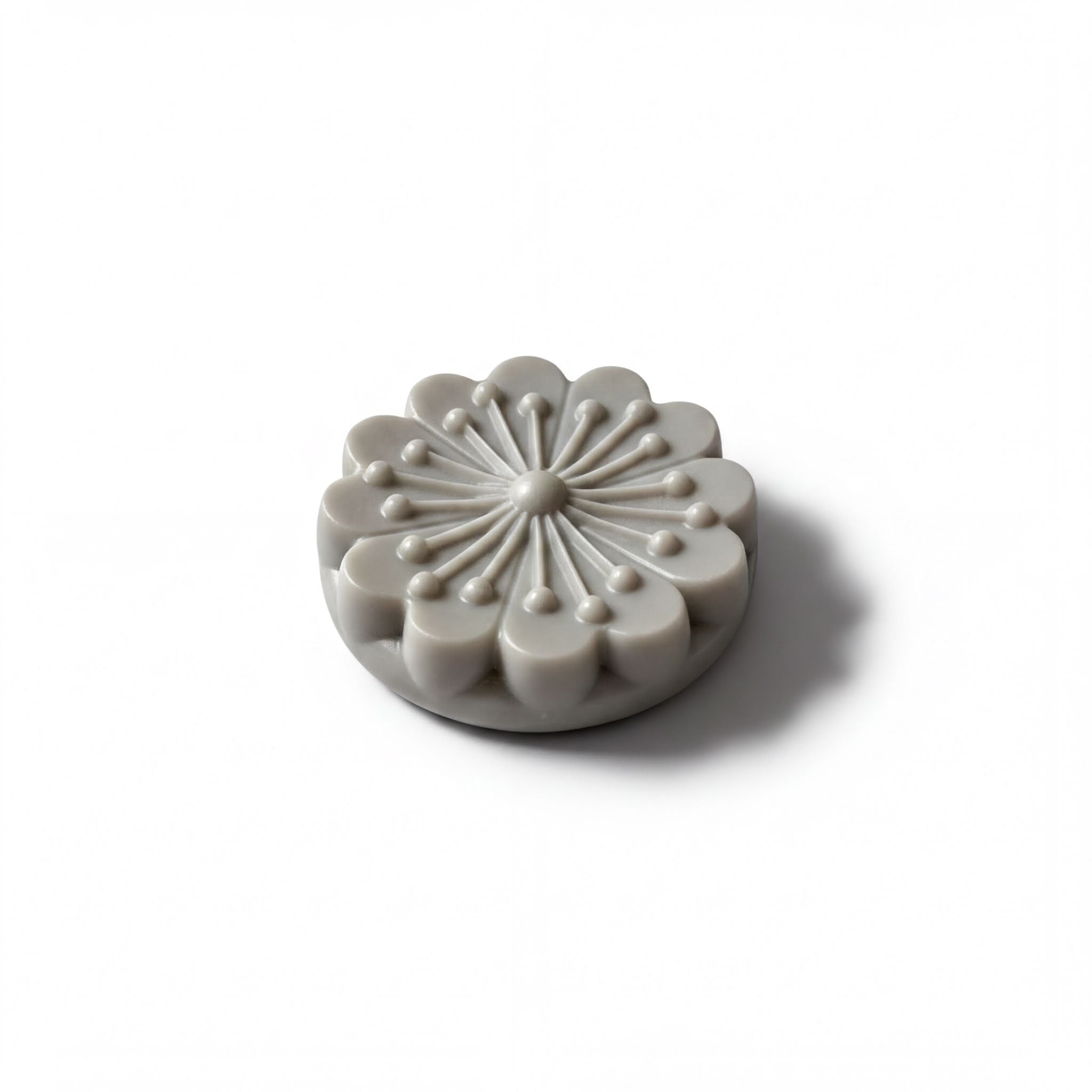 A gray, flower-shaped object with a central design and radiating petals is shown against a white background.