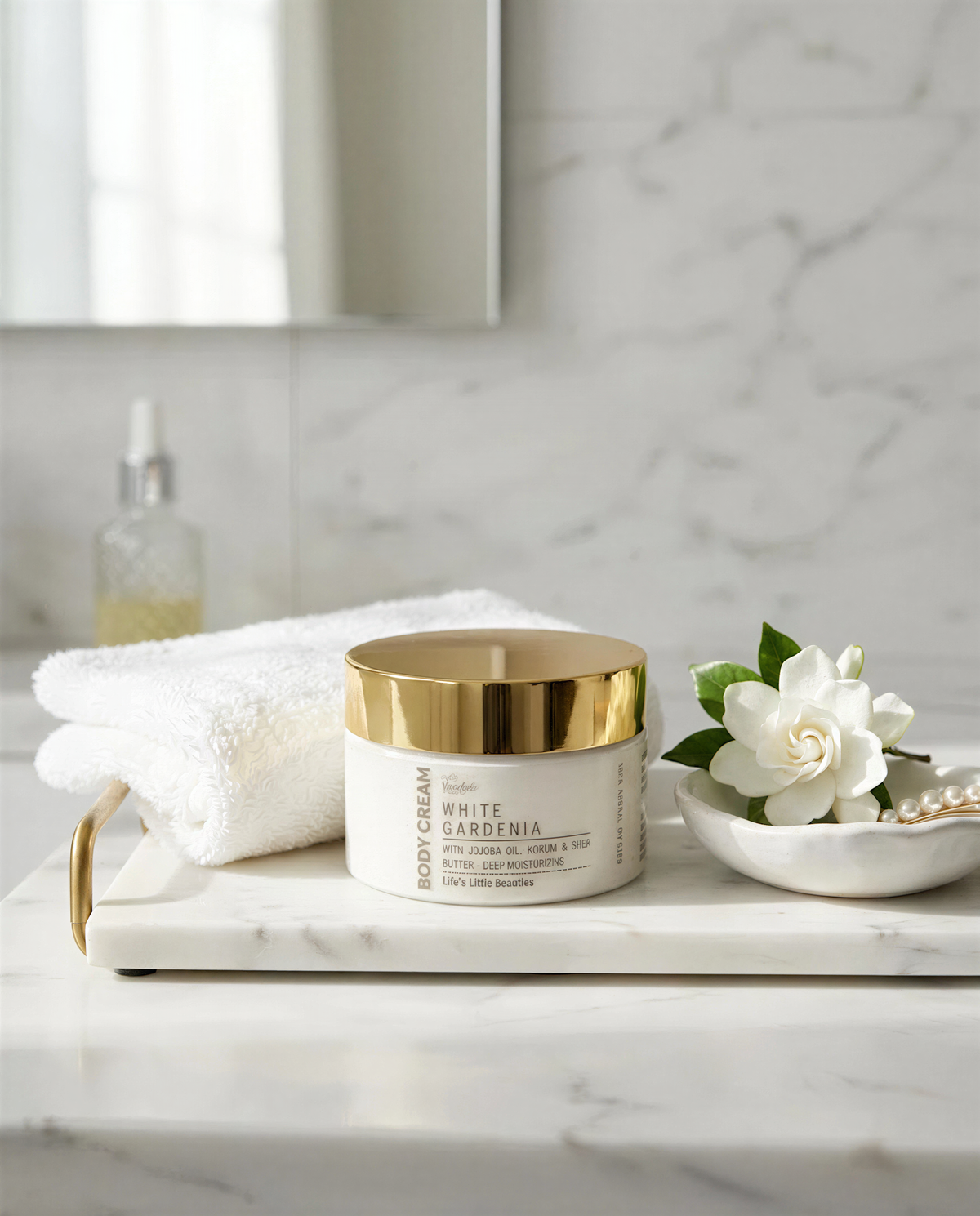 a white jar of body cream with a gold lid, placed on a marble countertop next to a white towel and a small white bowl containing a white flower.