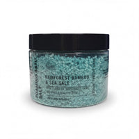 A jar of "Rainforest Bamboo & Sea Salt" with a black lid, containing a light blue-green substance that appears to be a natural exfoliant.