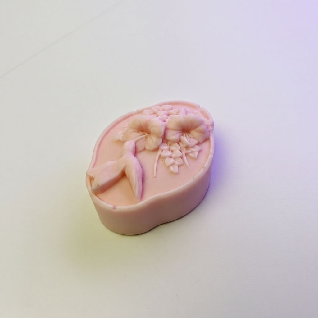 A pink, oval-shaped soap with a floral design on it, sitting on a white surface.