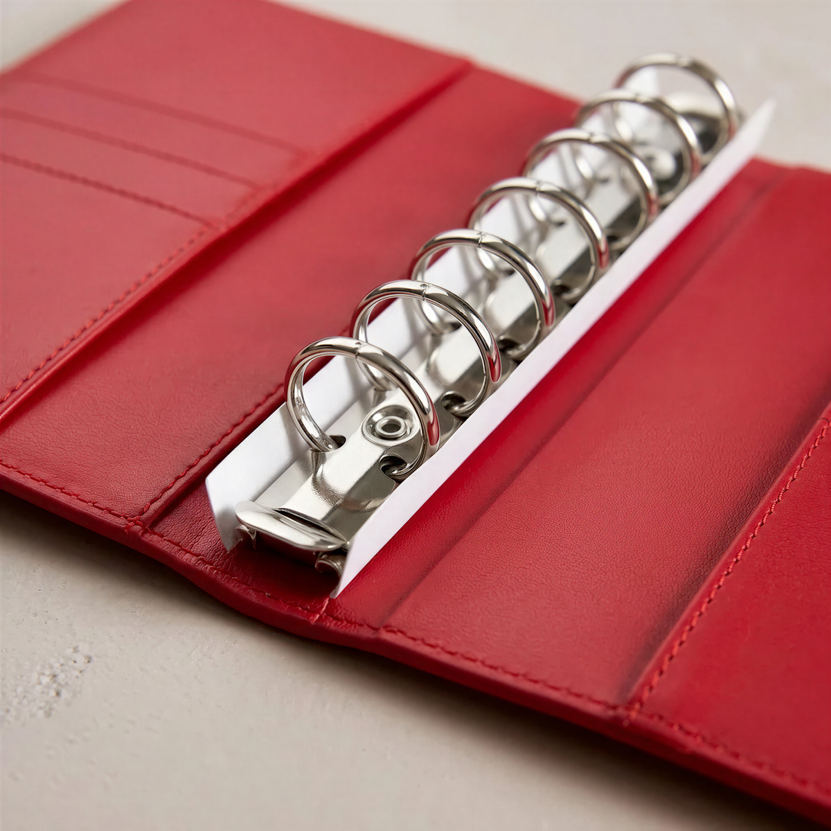 A red leather binder with a spiral-bound metal ring, placed on a white surface.
