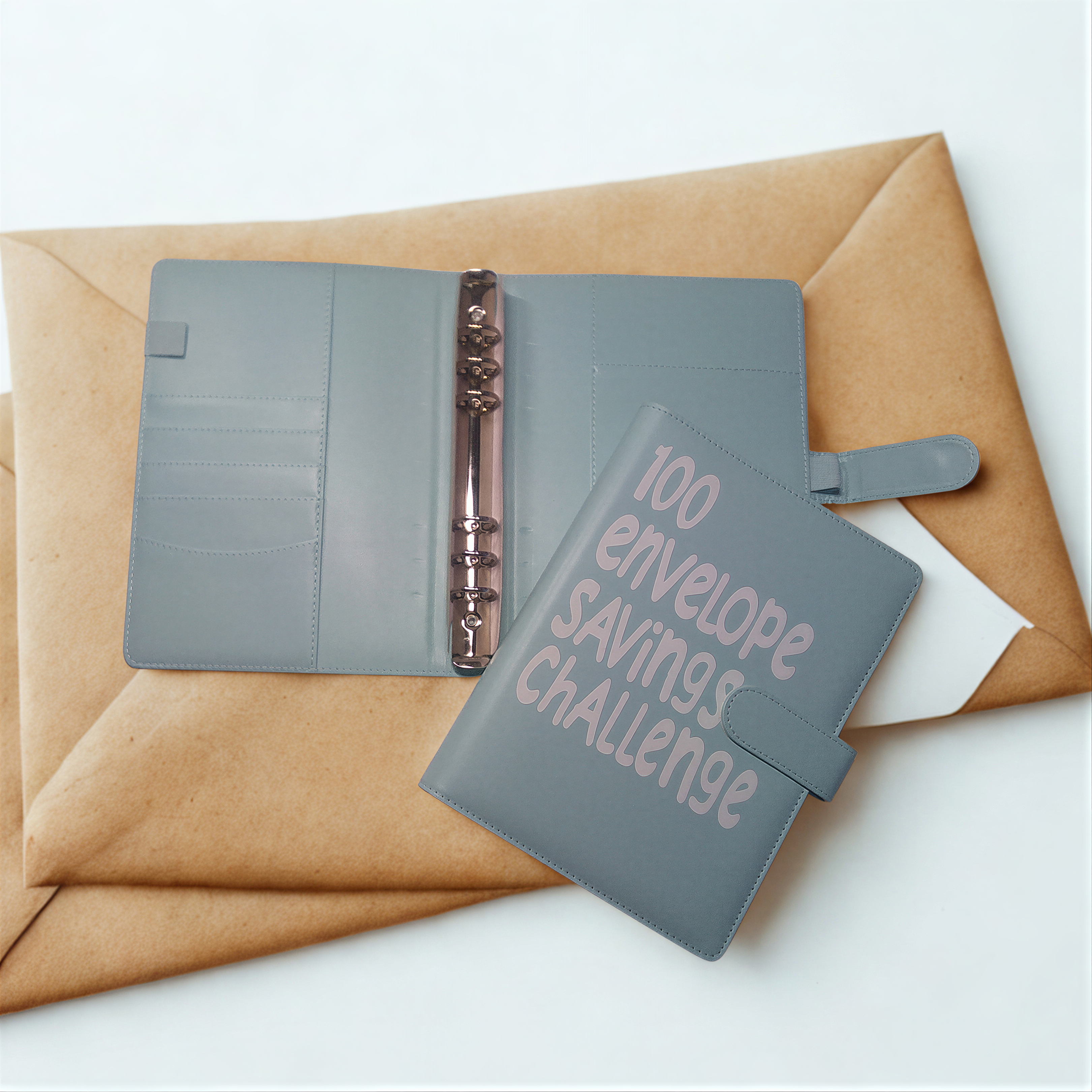 Gray 100 envelope savings challenge planner with ring binder on brown envelopes