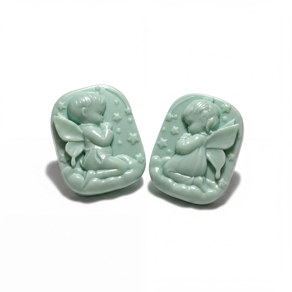 Two light green ceramic charms depicting cherubs or angels, each with wings and stars, are shown against a white background.
