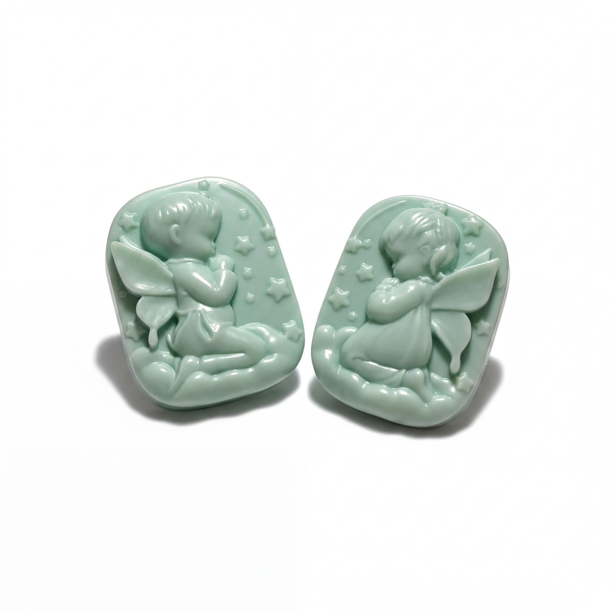 Two light green ceramic charms depicting cherubs or angels, each with wings and stars, are shown against a white background.