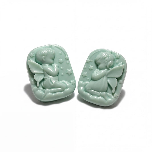 Two green soapstone charms depicting angelic figures are shown against a purple background.