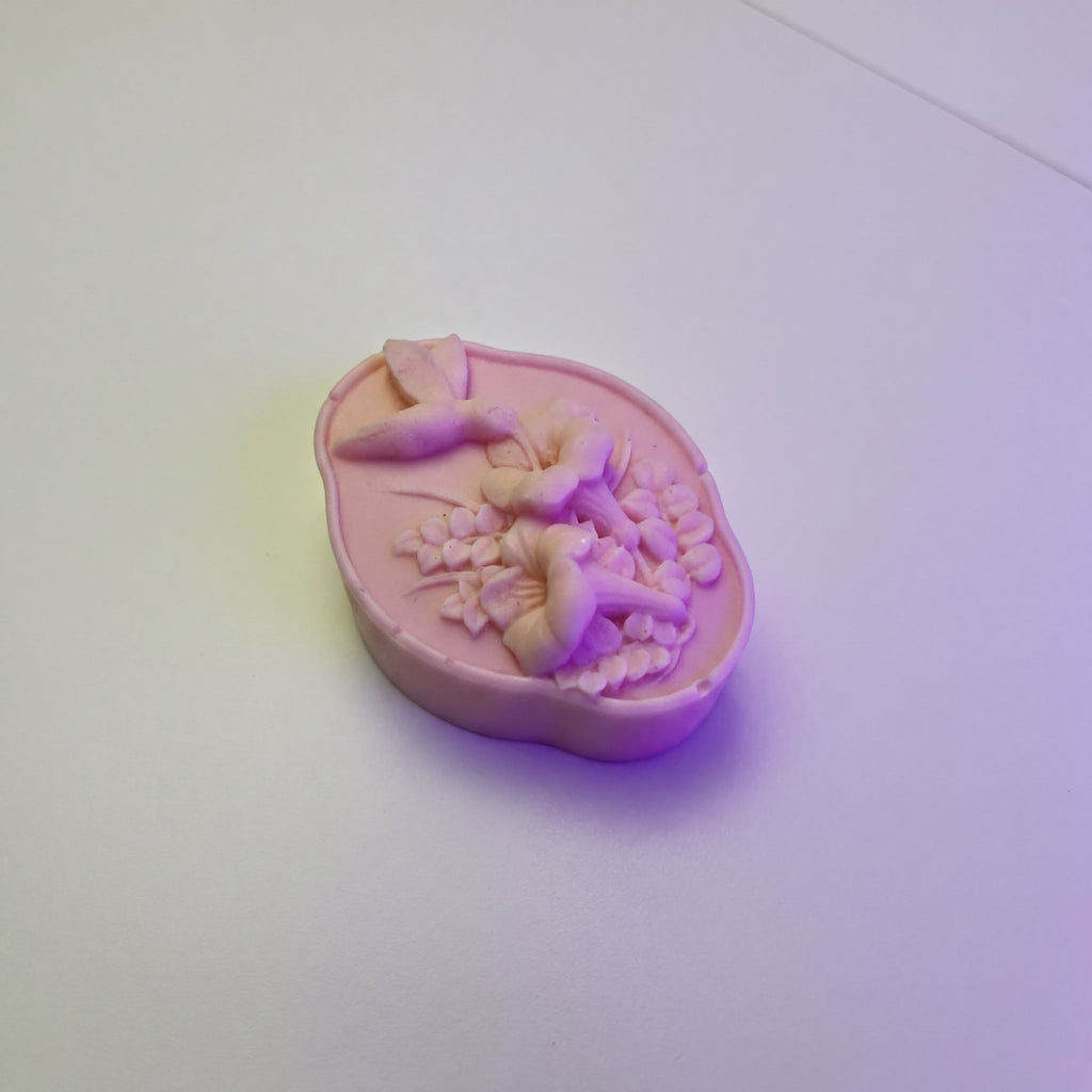 A pink soap bar with a floral design on it, sitting on a white surface.