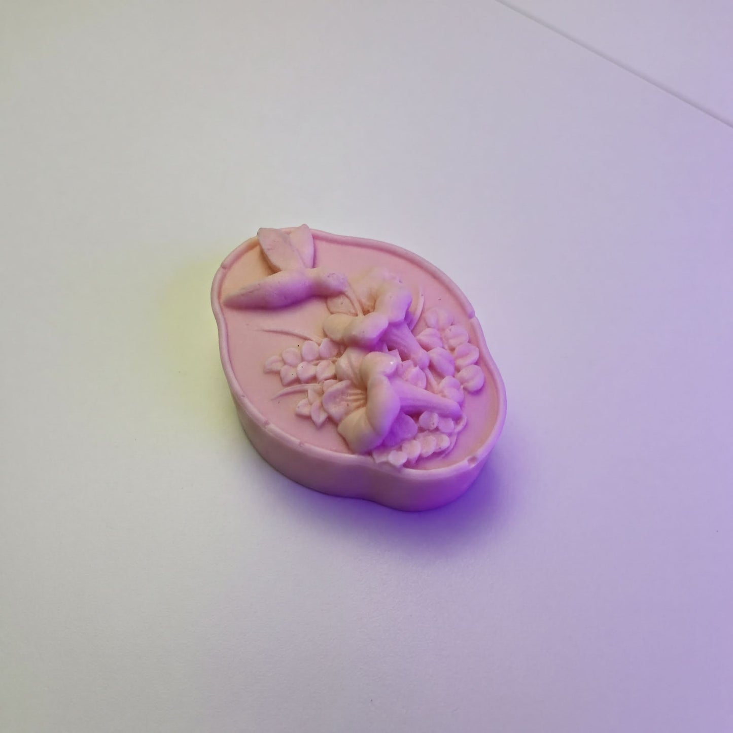 A pink soap bar with a floral design on it, sitting on a white surface.