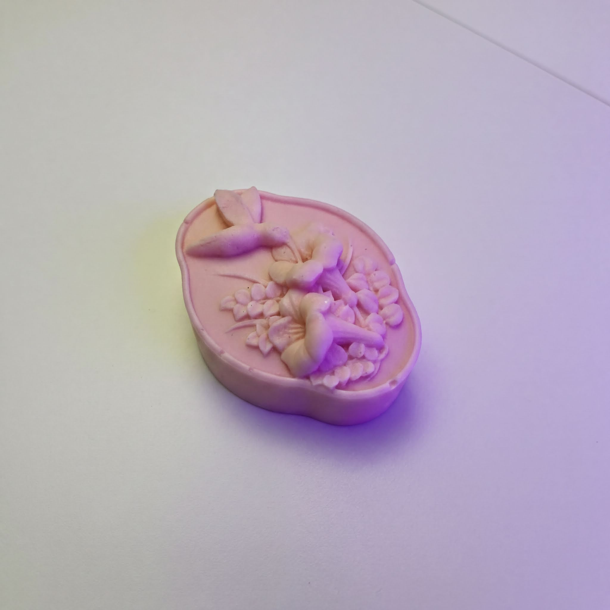 A pink soap bar with a floral design on it, sitting on a white surface.