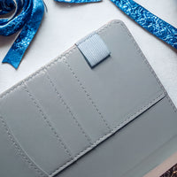 A close-up view of a gray wallet or card holder with a blue ribbon and other ribbons in the background.