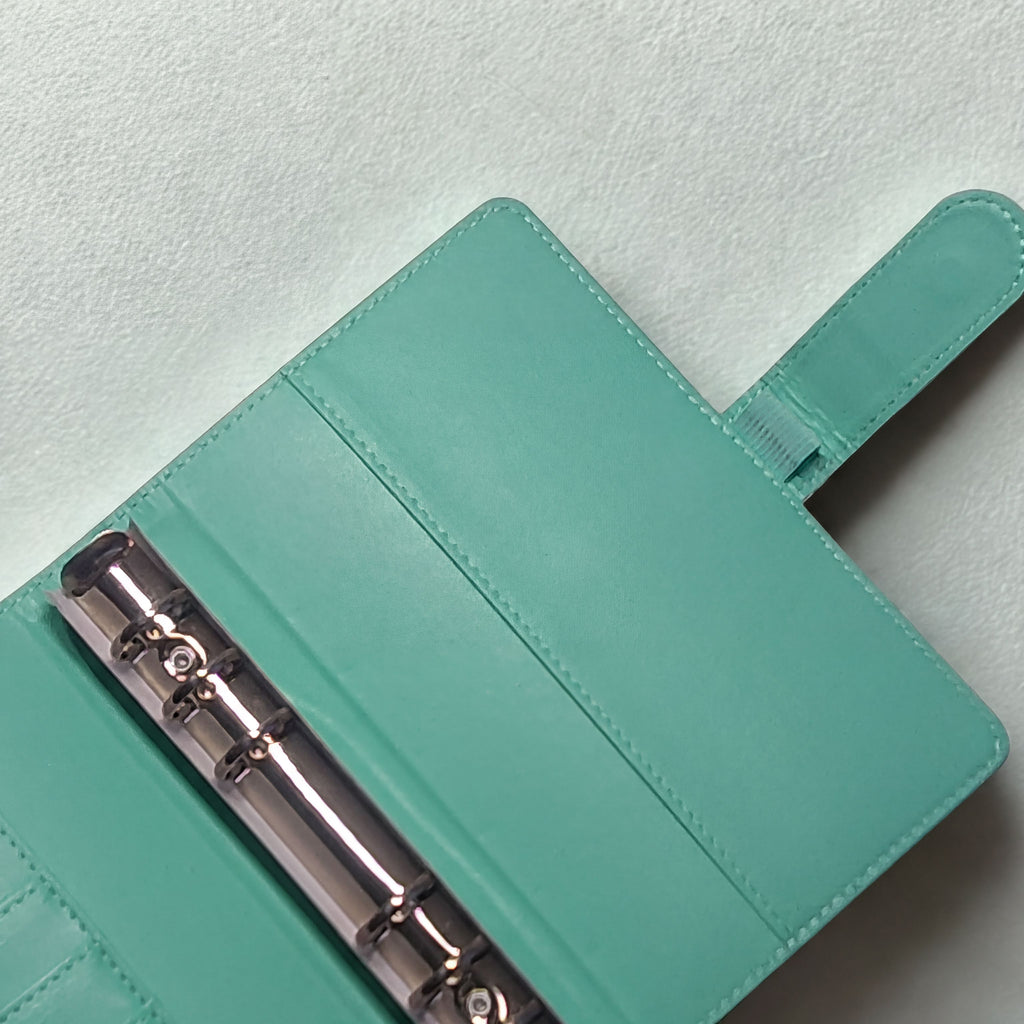 Mint green leather planner with silver binding, open on textured white surface