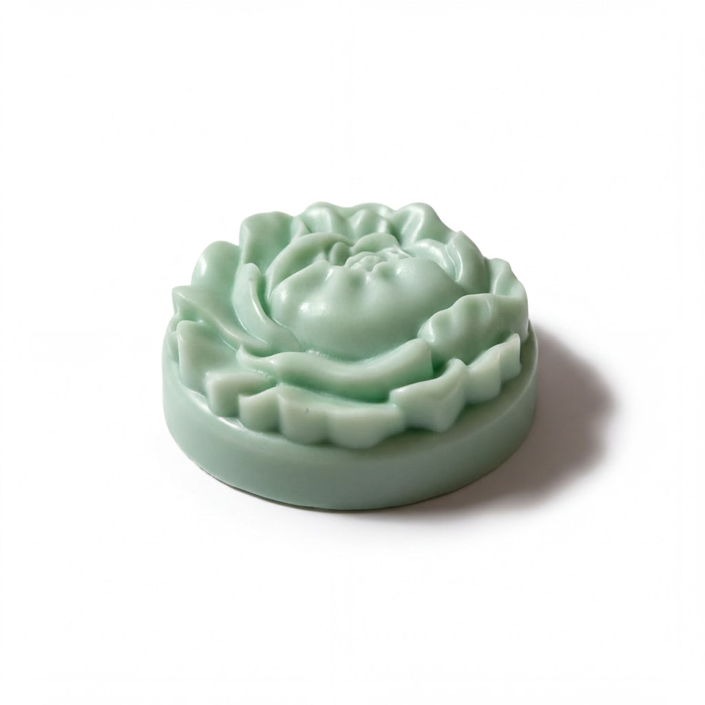 A green, round soap with a flower-like design sits on a white background.