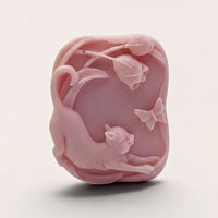 A pink soap bar with a cat and butterflies carved into it.
