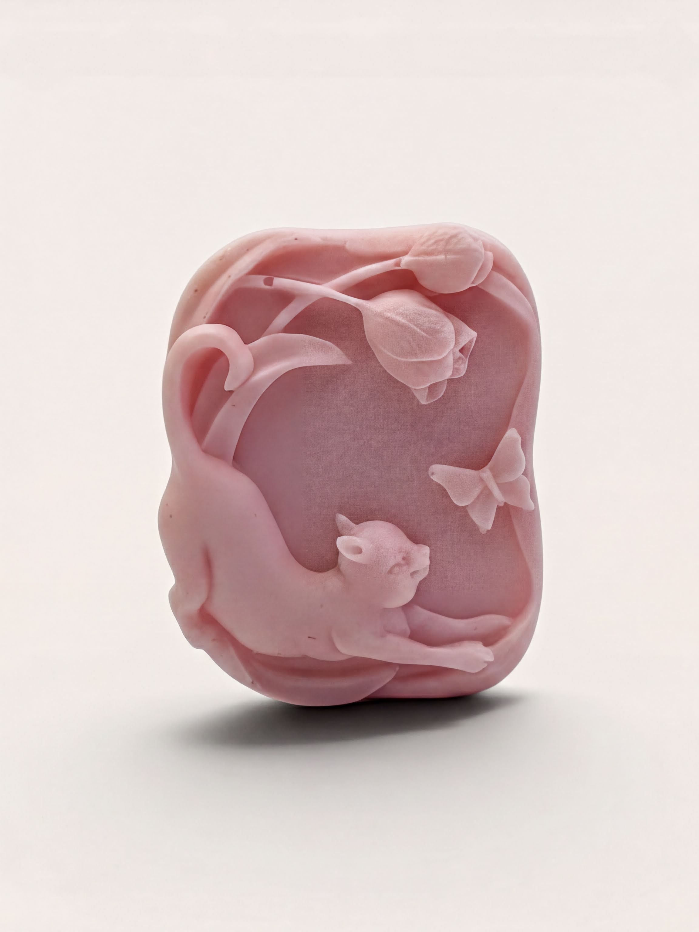 A pink soap bar with a cat and butterflies carved into it.