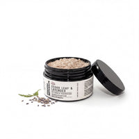 A jar of bath salt with a black lid, containing a mixture of brown and white grains, and a sprig of lavender.