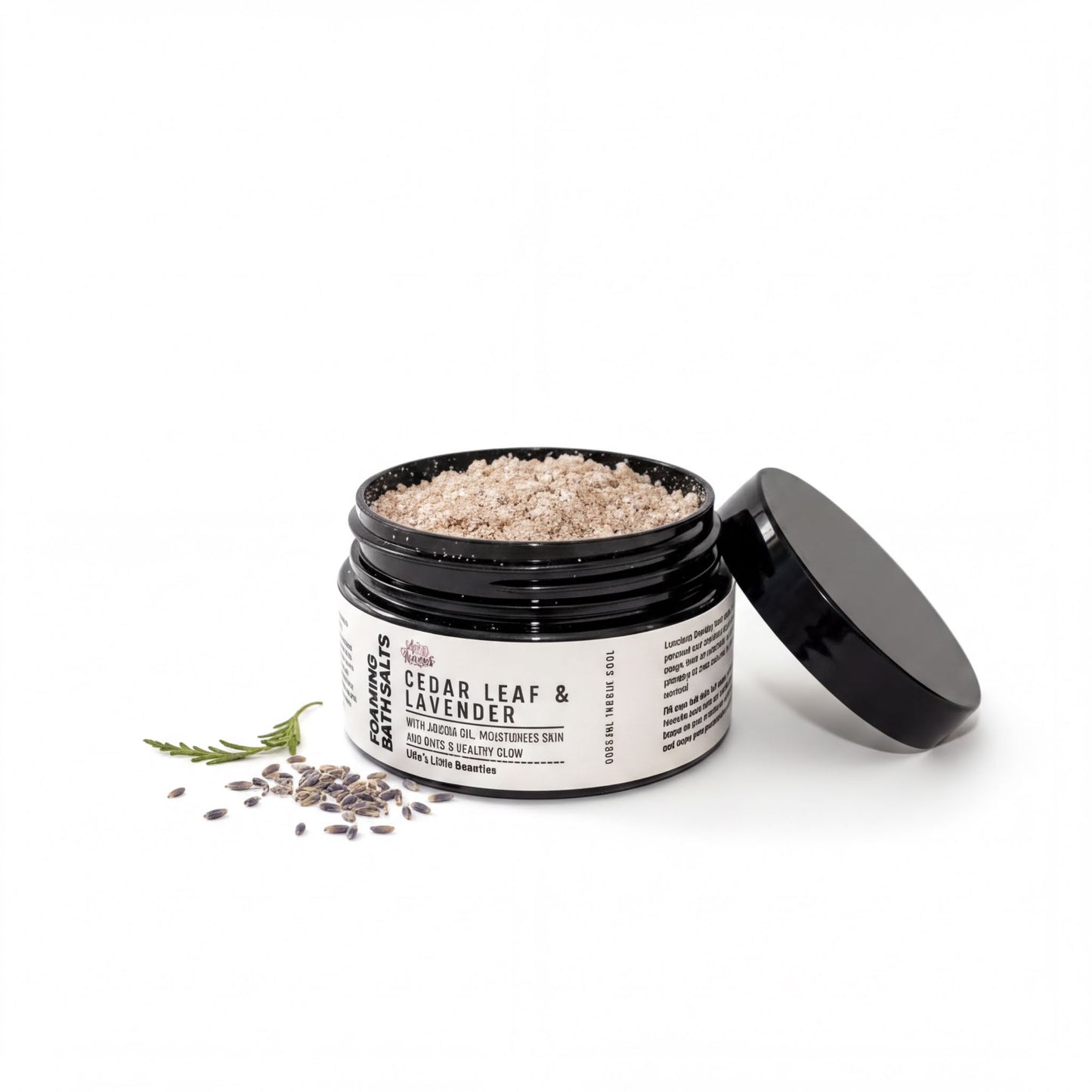 A jar of bath salt with a black lid, containing a mixture of brown and white grains, and a sprig of lavender.