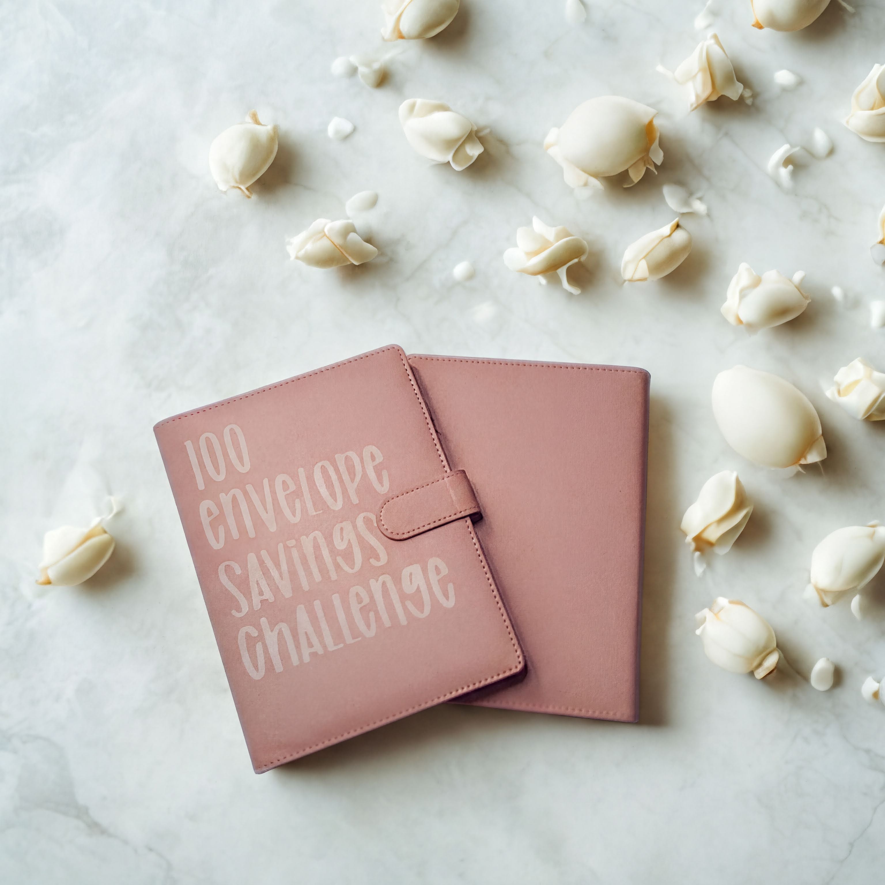 Pink 100 envelope savings challenge booklet on marble with white rose petals